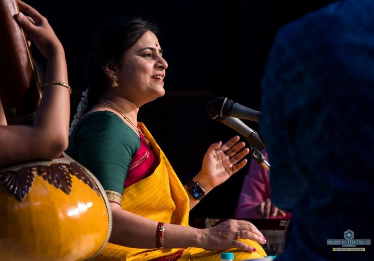 Bharathi Prathap singing, sitting cross-legged and wearing colourful clothes