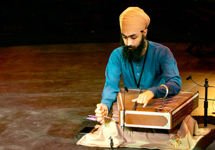 Eeshar Singh playing the santoor - a flat stringed instrument. He is wearing a beige turban and blue shirt.