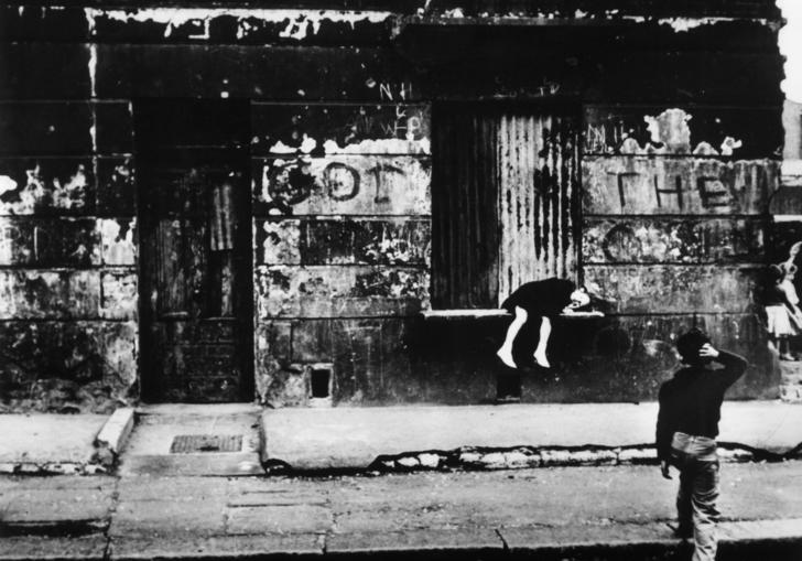 A black and white photograph of a street with god save the queen written in graffiti on the wall