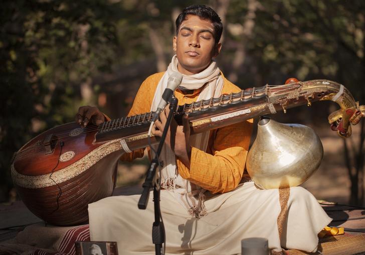 Ramana Balachandran sitting in a garden playing his veena - a large stringed instrument