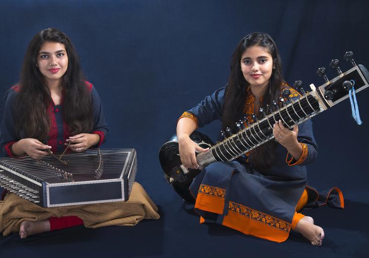 Sanskrati and Prakrati Wahane playing their instruments in front of a dark background