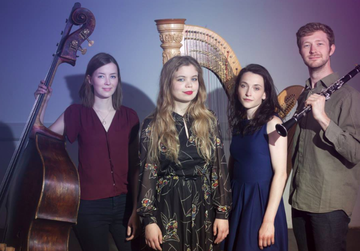 The Hermes Experiment standing with their instruments: a double bass, a clarinet and a harp