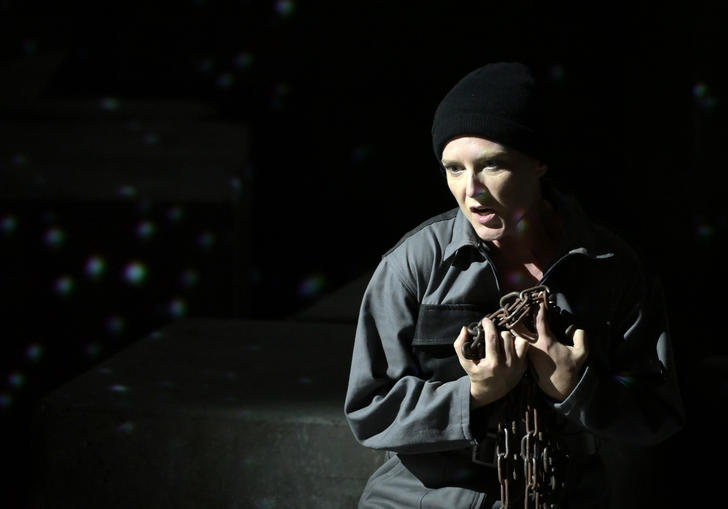 Sinead Campbell-Wallace performs as Leonore, wearing a prison jumpsuit and holding shackles