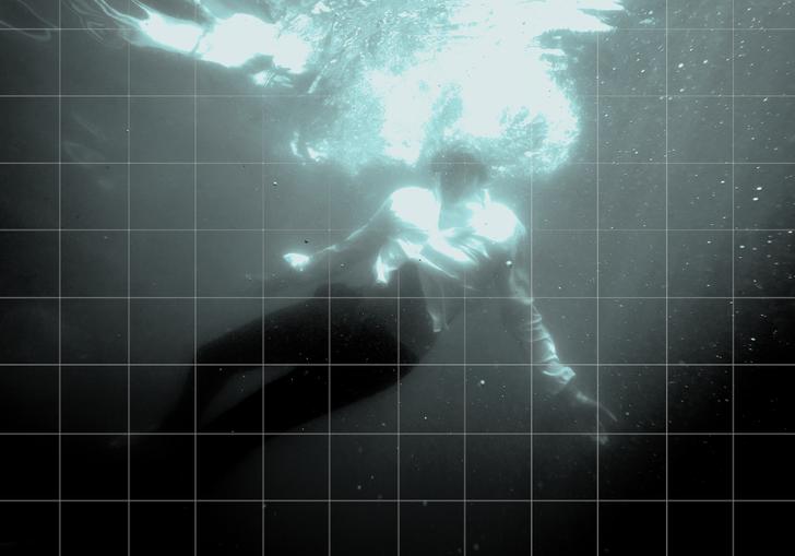A man in a white shirt and black trousers is underwater with his arms outstretched