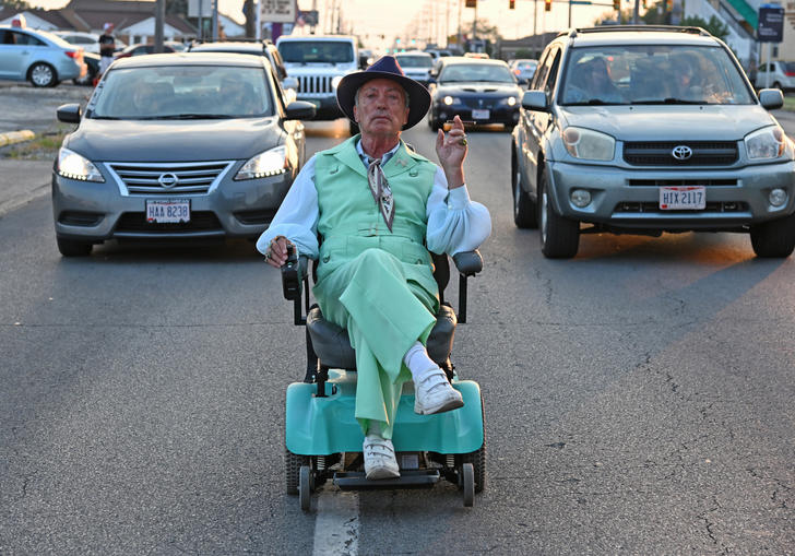 A well dressed man in a mobility chair in front of cars on a motorway in a still from Swan Song