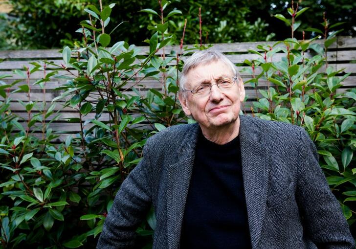 John Cumming wearing a dark suit, in front of a bush and fence