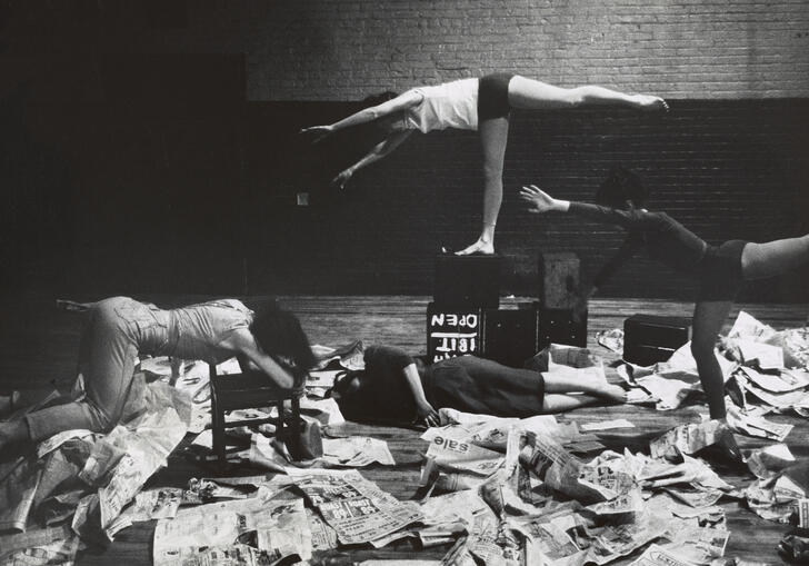 Image shows 4 dancers posing horizontally amongst newspapers 