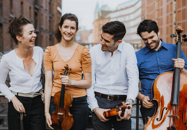 The Aris Quartett standing on a bridge holding their instruments