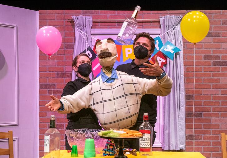Bill, a large puppet with a moustache, is moved by two puppeteers dressed in black. There are balloons and a happy birthday banner behind them.