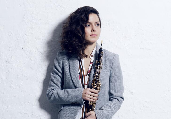 Cristina Gomez Godoy standing in front of a white wall holding her oboe
