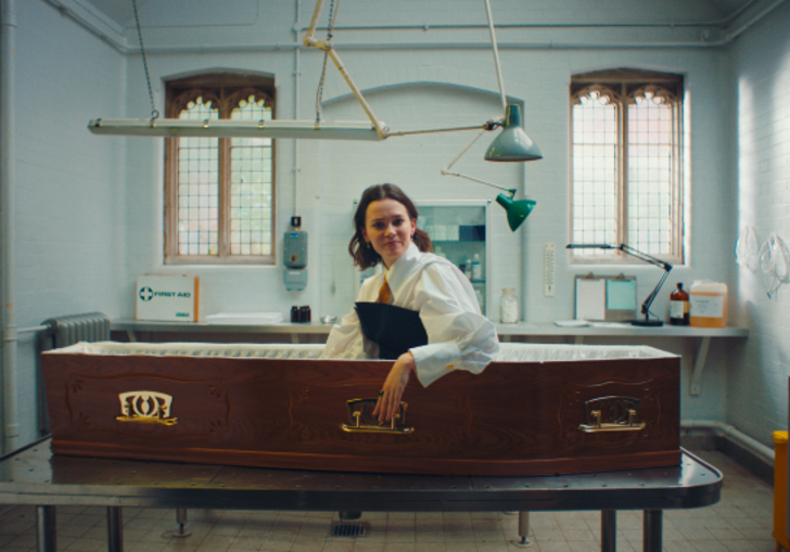 Person sits upright in coffin, camera from sideview.