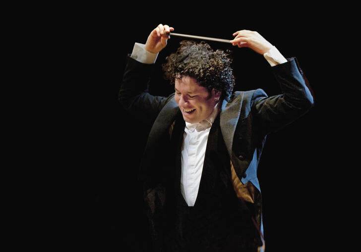 Gustavo Dudamel smiling while holding his baton above his head