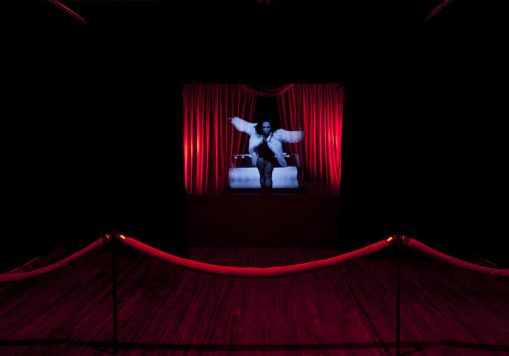 Woman in blue light on the middle of a stage with red curtains on either side