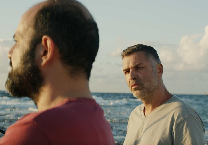 Two men speak near a body of water 