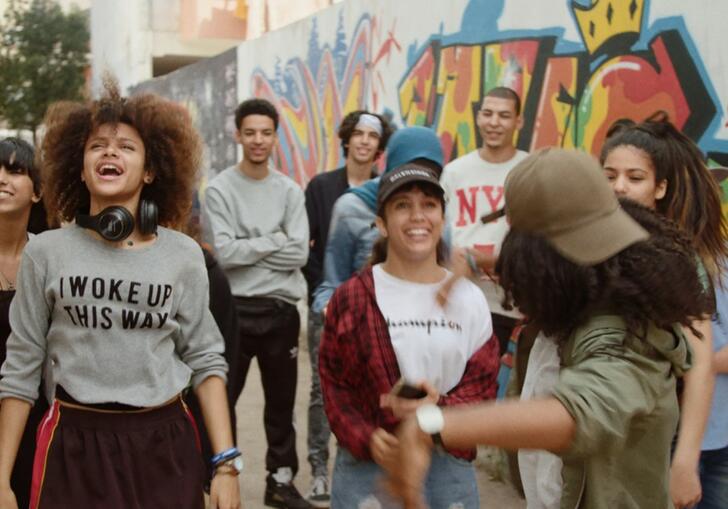 group of young people walking in the street laughing standing in front of a graffiti wall