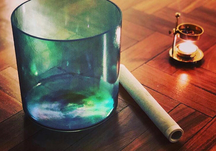 Image of a green glass sat upon a wooden table next to a long stick and candle