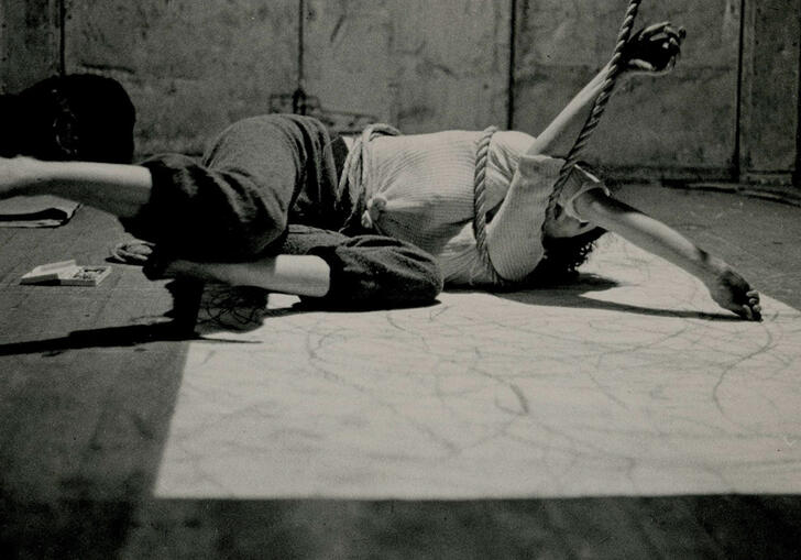 Black and white image with a human body entangled in rope on the floor