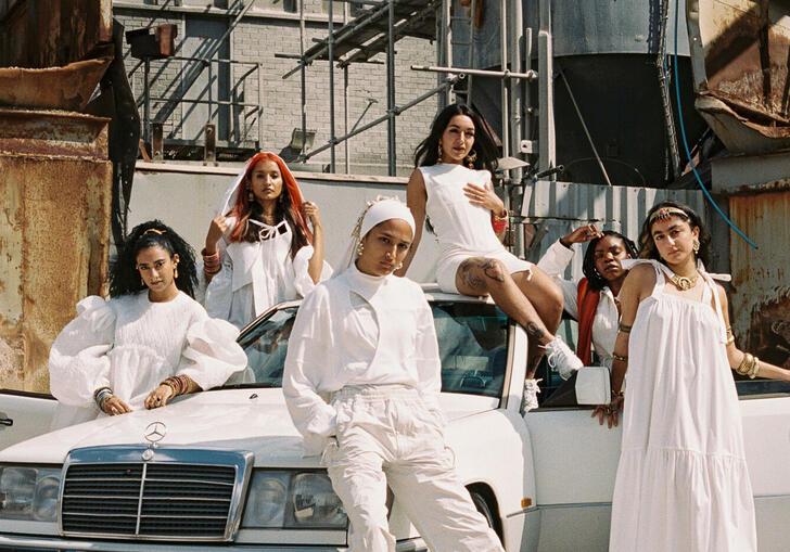 A group of people stand around a car, all dressed in white, looking to camera