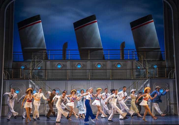A group of people dance in front of a ship