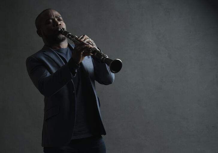 Anthony McGill playing his clarinet in front of a grey background