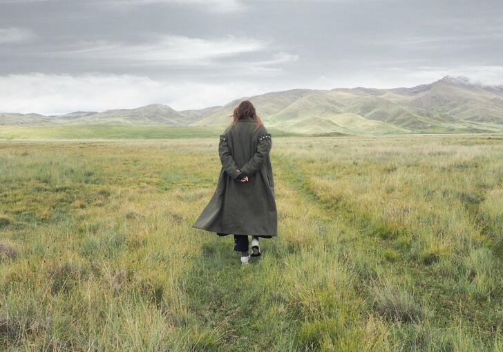 Women standing in field with long black coat.