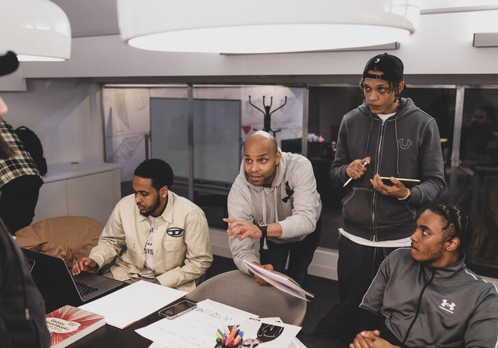 People sit across from one another over a table, designing something on paper.