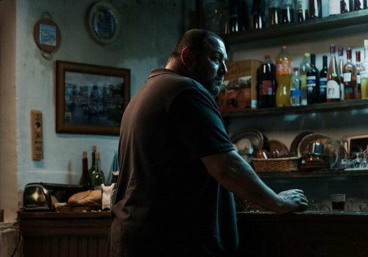 A man stands at a bar and looks broodingly over his shoulder in a still from The Beasts.