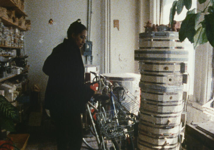A woman stands in front of a window by a bike and film reels in a Still from Finding Christa.
