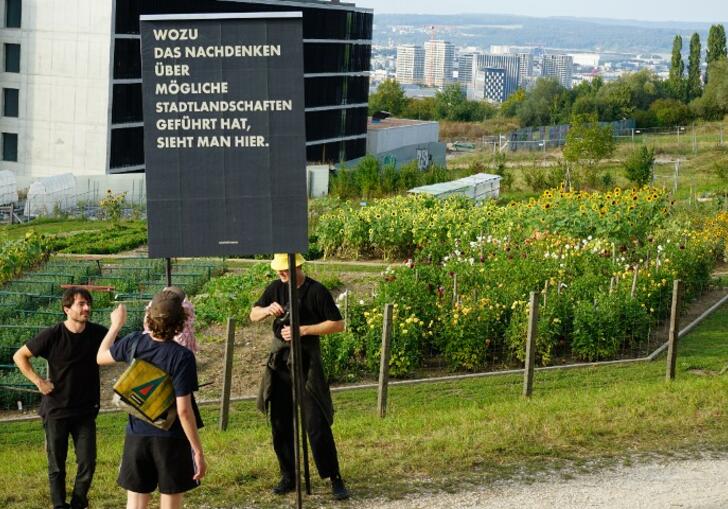 photo of three people standing outside a building holding a sign written in German