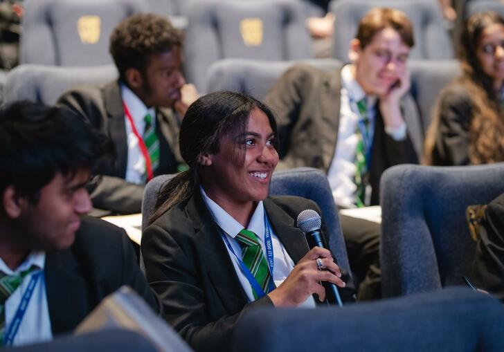 Image of student wearing blazer and green tie holding microphone