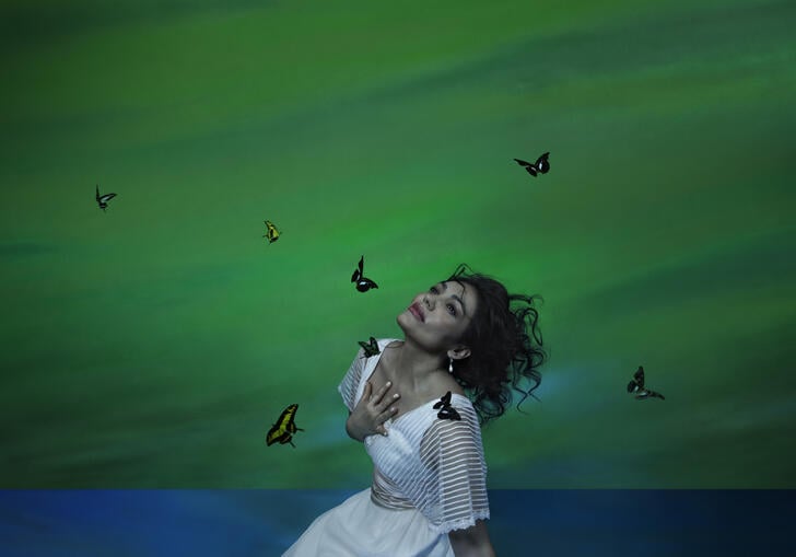 A woman neels down in a white dress, surrounded by butterflies