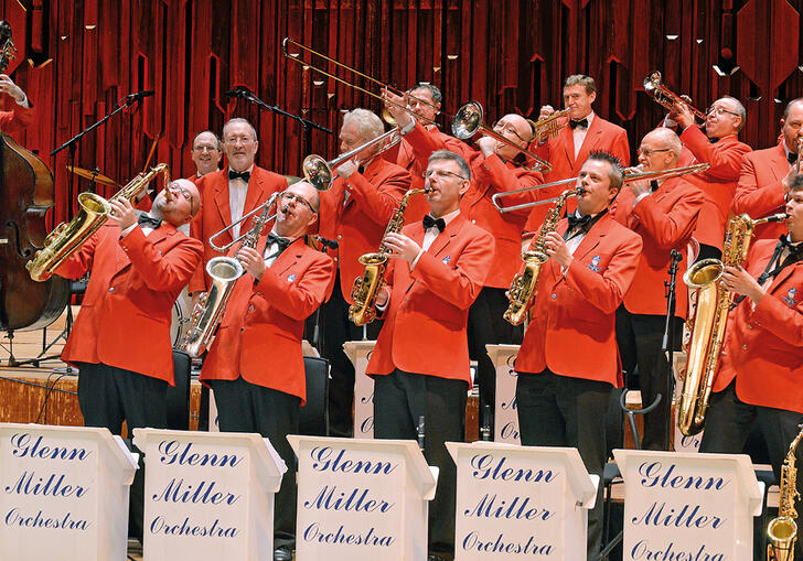 The brass section of the Glenn Miller Orchestra performing on stage, with the double bassist in the background