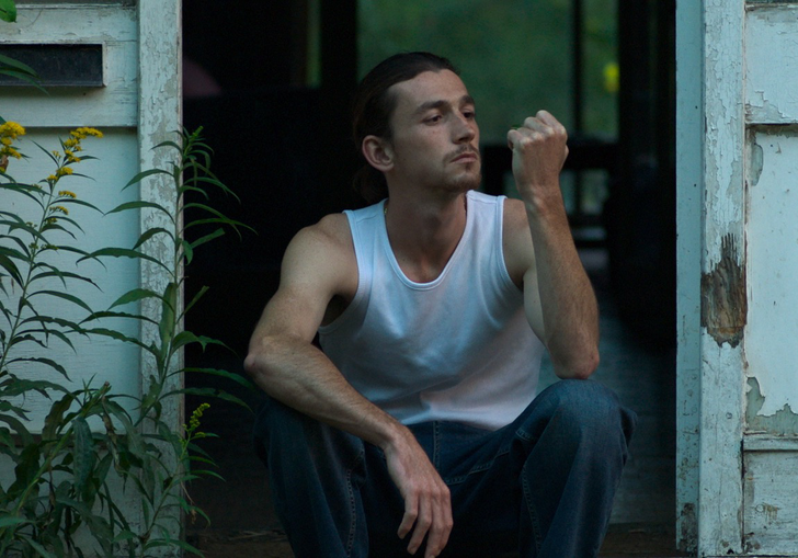 A man sits in a peeling doorway at dusk