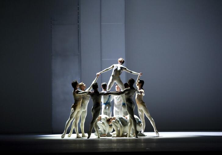 A group of dancers rise up together on a minimal stage