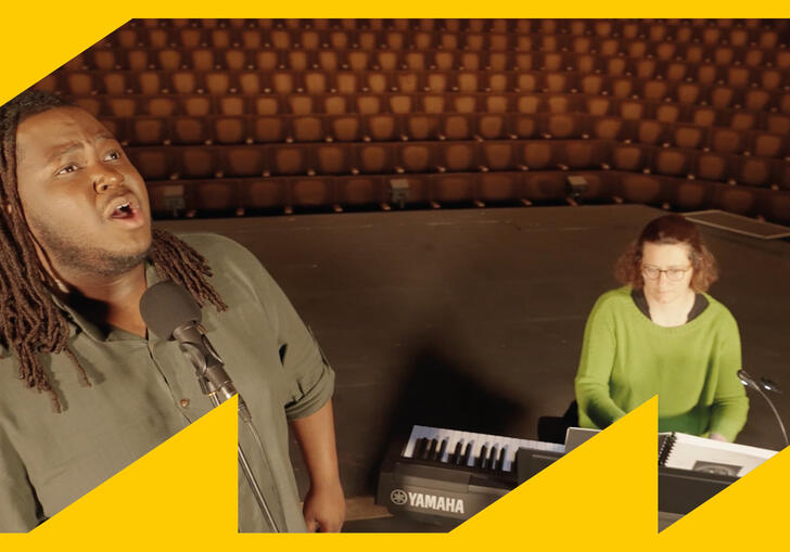 An image with two people, one is further away playing the piano while the other is closer to the camera, looking up wards and singing.