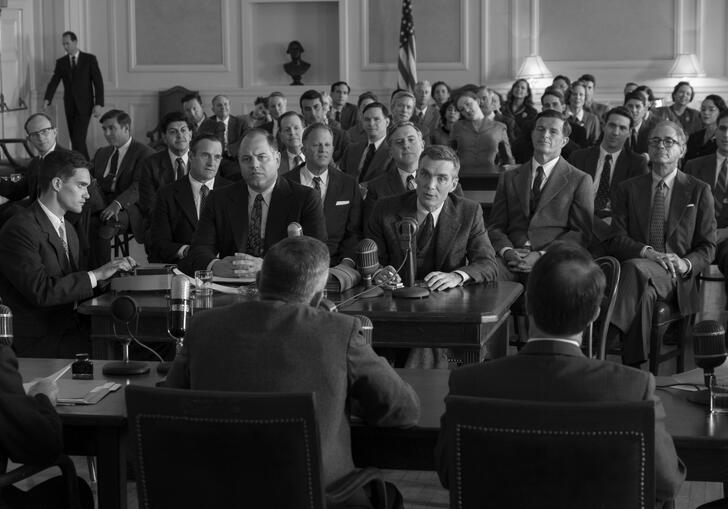 Oppenheimer sits in a room full of men wearing 1940s suits