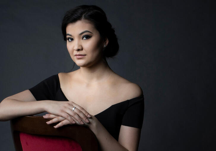 A woman in a black top sits in a chair looking intensely forward