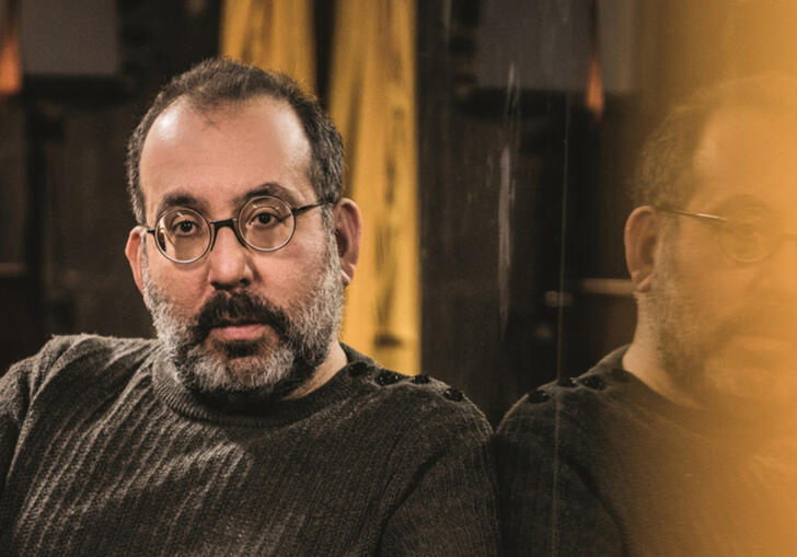 A man with a beard and glasses sits in a room looking forward