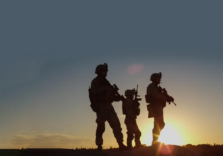 Three soldiers standing in silhouette against sunrise