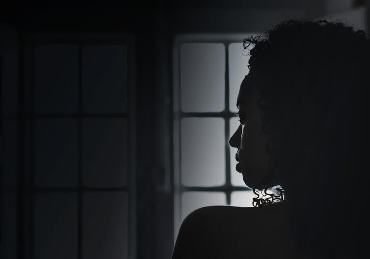 Silhouette of woman in profile looking over her shoulder in dark room with window in background