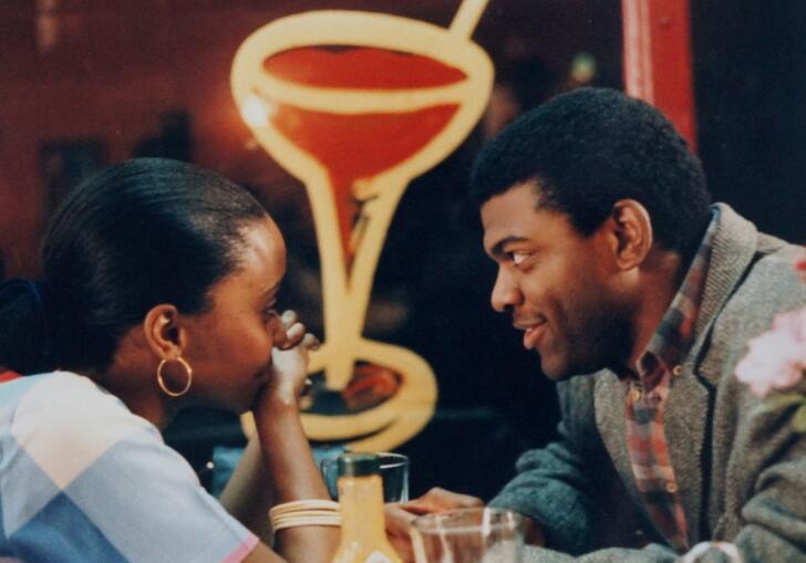 A man and a woman sit close opposite each other in a New York diner