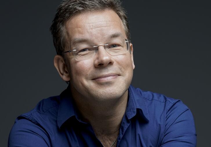 Antony Hermus smiling at camera wearing blue shirt and glasses