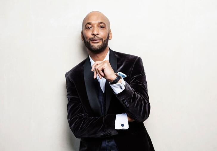 Tommy Blaize wearing black velvet jacket looking at camera with one hand near 
