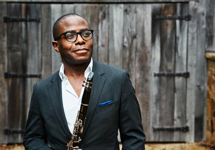 Anthony McGill standing in front of a wooden barn holding his clarinet