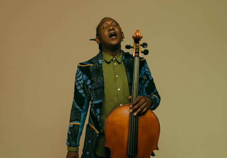 Abel Selaocoe looking upwards with his eyes closed, holding his cello 