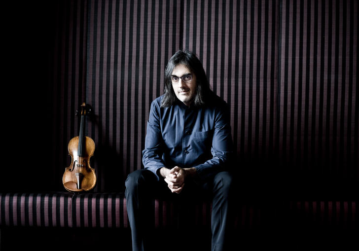 Leonidas Kavakos with his hands clasped sitting on a bench, his violin standing upright next to him