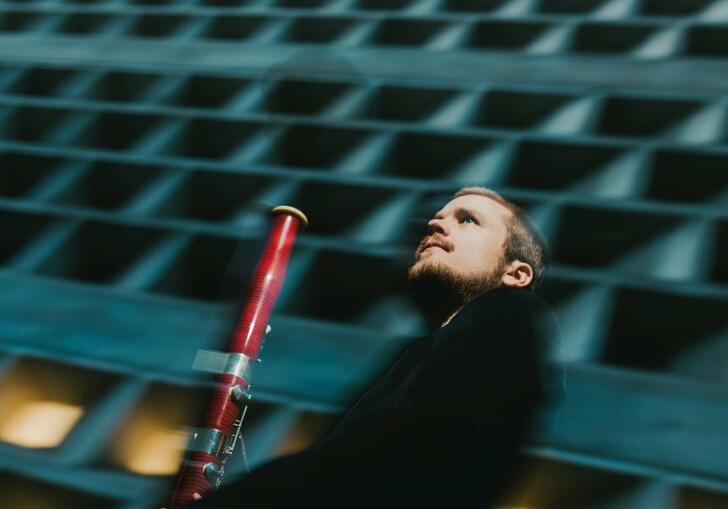 Mathis Stier holding his bassoon in front of a concrete building