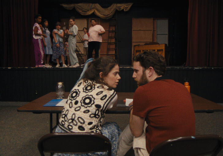 Two theatre leaders discuss a young performer on stage