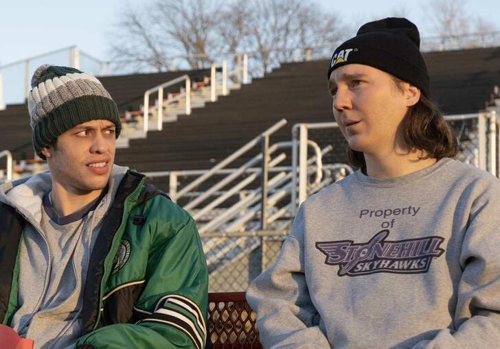 Two young men sit on bleachers looking at each other.