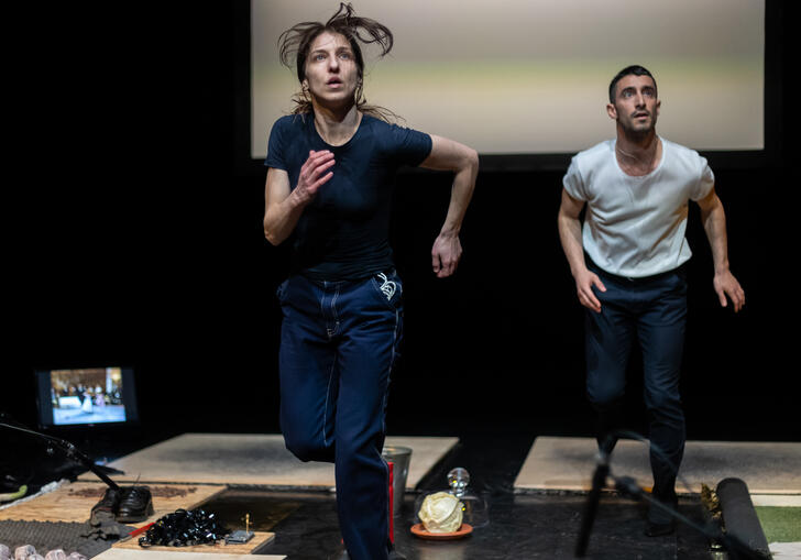 Two dancers run on treadmills... they look out at the audience, watching something, concerned.